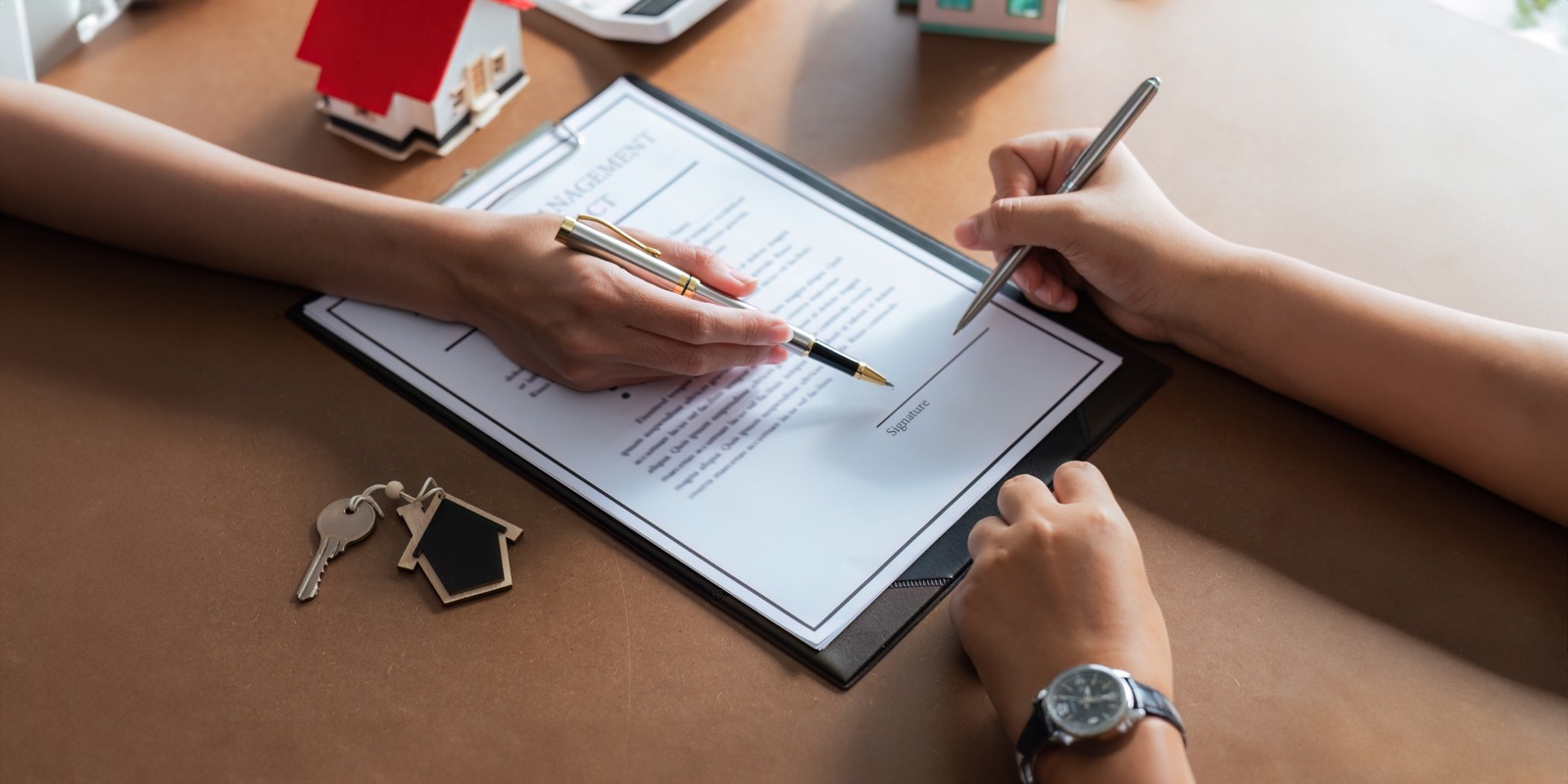 A tenant signing a lease agreement with house keys on the table